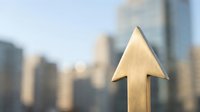 Golden wooden arrow pointing upward against blurred city skyline background symbolizing growth, success, progress and business achievement concepts.