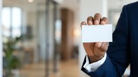 Businessman with dark skin tone holding blank white business card in modern office environment with blurred background, suitable for corporate branding and professional marketing materials.