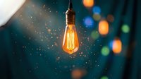 Vintage Edison light bulb glowing with warm filament against dark teal background with bokeh lights, suitable for energy, innovation, and creative concept designs.