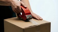 Caucasian male hands sealing cardboard box with red tape dispenser against white background for shipping, packaging, and logistics concepts.