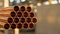 Stack of shiny copper pipes in industrial warehouse setting with blurred background lights for construction and plumbing projects.