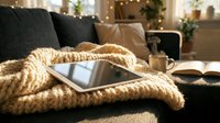 Cozy living room scene with tablet and warm knitted blanket on sofa. Comfortable home interior with soft lighting for relaxation and digital lifestyle.