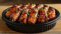 Glazed chicken wings with sweet and spicy Asian sauce garnished with sesame seeds and green onions served in black plate on wooden table, appetizing party food.