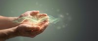 Cupped hands holding glowing energy light with magical particles floating in dark atmospheric background for spiritual healing and wellness concepts.