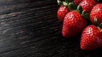 Fresh ripe strawberries with green leaves on dark rustic wooden background with copy space. Natural light food photography for menu design and marketing.