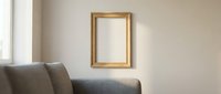 Elegant gold picture frame hanging on a neutral beige wall in a modern living room interior with soft natural light and sofa.