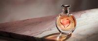 Elegant glass perfume bottle with amber fragrance on marble surface with soft natural lighting creating warm shadows and luxurious cosmetic product display.