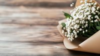 Delicate white baby's breath flowers wrapped in beige craft paper on rustic wooden background. Romantic floral arrangement with soft natural lighting and copy space.