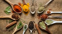 Colorful spices and herbs arranged in wooden spoons on rustic table. Cooking ingredients including turmeric, paprika, coriander seeds for culinary recipes.