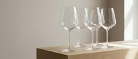 Five elegant crystal wine glasses arranged in row on wooden surface with soft natural lighting and neutral background for dining and entertaining.