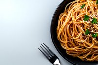 Spaghetti pasta with sesame seeds and fresh herbs served in black plate on white background. Fork beside plate creates minimalist food composition.