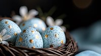 Speckled blue Easter eggs with gold spots nestled in woven nest with white spring flowers, creating festive holiday atmosphere against dark background.