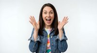 Excited young Caucasian woman with long brown hair raising hands in surprise gesture wearing denim jacket on white background for marketing campaigns.