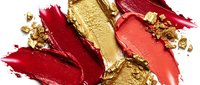 Luxurious red, coral, and gold lipstick smears with crushed metallic flakes on white background, showcasing bold makeup textures.