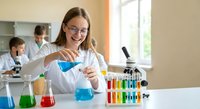 Young female scientist in white lab coat conducting chemical experiment with colorful solutions in modern laboratory setting for educational research.