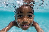 Young African American boy swimming underwater with bright smile, face close-up showing joy and playfulness in clear turquoise pool water with bubbles.