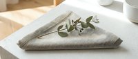 Folded beige linen napkin with fresh eucalyptus sprig on white plate, styled for dining, events, and table setting design projects.