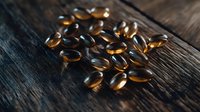 Omega-3 fish oil capsules scattered on dark wooden surface in moody lighting, highlighting golden translucent supplements for health and wellness content.