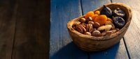 Wicker basket filled with assorted nuts and dried fruits on rustic wooden table. Healthy snacking, organic food ingredients for cooking and baking recipes.