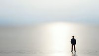Lone figure silhouette standing on reflective surface against bright minimalist background creating contemplative atmosphere for meditation concepts.