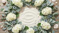 White hydrangea flowers and eucalyptus leaves arranged in circular wreath on rustic wooden background with seashells for wedding decor and home styling.