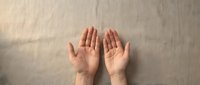 Open hands gesture on neutral beige fabric background showing palms up in receiving or offering position for wellness and spiritual concepts.
