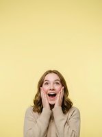Young woman with shoulder-length brown hair and fair complexion expressing surprise and excitement with hands on cheeks against yellow background for advertising and lifestyle campaigns.