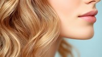 Close up profile of young caucasian woman with wavy blonde hair and natural makeup showing plump lips against blue background, beauty and cosmetics concept.