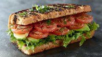Fresh submarine sandwich with layers of sliced tomatoes, crisp lettuce on toasted bread garnished with herbs and seasonings. Appetizing lunch meal.