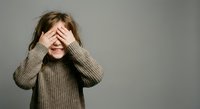 Young blonde woman covering eyes with hands wearing beige knit sweater expressing surprise shame or playing peek-a-boo game against neutral background.