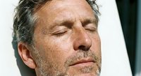 Middle-aged Caucasian man with closed eyes and gray beard in peaceful meditation pose against white background for wellness and mindfulness concepts.