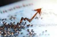 Rising golden arrow emerges from scattered metallic fragments against blurred financial chart background, symbolizing business growth and market recovery.