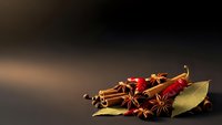 Aromatic spices including cinnamon sticks, star anise, bay leaves and chili peppers arranged on dark surface for culinary and cooking projects.