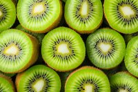 Fresh sliced kiwi fruit arranged in rows showing bright green flesh and black seeds in a repeating pattern, close-up macro photography for food design.