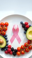 Pink ribbon surrounded by fresh healthy foods including avocado, berries, and tomatoes on white plate promoting cancer awareness and nutrition.
