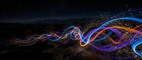 Abstract flowing light trails with colorful neon waves and particles against dark starry night sky background for digital art and futuristic designs.