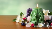 Spa wellness setup with green carved candle, healing crystals, amethyst cluster and white flowers on wooden surface for relaxation therapy.