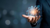 Businessman hand holding glowing house icon with percentage symbol and upward arrows representing real estate investment growth and mortgage rates.