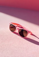 Stylish pink sunglasses with dark lenses on pastel pink surface with dramatic shadows and red background, perfect for summer fashion content.