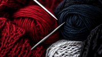 Red and navy blue yarn balls with silver knitting needles in dramatic lighting, creating contrast between warm and cool tones. Close-up macro photography highlights textile texture.