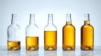 Bottles of whiskey, brandy, or bourbon showing progressive fill levels from empty to full with golden amber liquid, arranged in a row for beverage, alcohol, or spirits concepts.