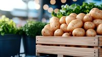 Fresh organic potatoes in wooden crate at farmers market with green herbs and soft bokeh lights in background, natural healthy produce display.