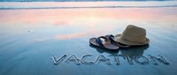 Flip flops and straw hat on wet sandy beach with vacation text written in sand at colorful sunset, summer travel and holiday concept.