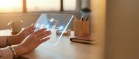 Professional woman using transparent holographic tablet display with futuristic interface technology in modern office workspace during golden hour lighting.