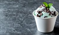 Mint chocolate chip ice cream topped with chocolate shavings and fresh mint leaf in white paper cup on dark marble background with copy space. Food photography.