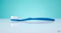 Blue toothbrush with white bristles on clean white surface against turquoise background for dental hygiene and oral care concepts.