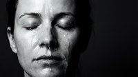 Middle-aged woman with closed eyes in contemplative expression, studio portrait against dark background, monochrome lighting for meditation and wellness concepts.