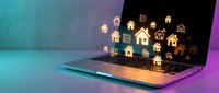 Digital real estate concept with golden house icons floating above laptop keyboard representing online property search and virtual home buying technology.