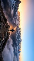 Silhouetted person standing on rocky cliff edge overlooking misty mountain valley at golden sunrise, dramatic landscape with layered peaks and atmospheric fog for travel and adventure concepts.
