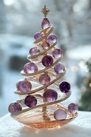 Elegant spiral Christmas tree ornament with purple amethyst spheres and gold metallic accents on snowy background with soft bokeh lights. Festive holiday decor.